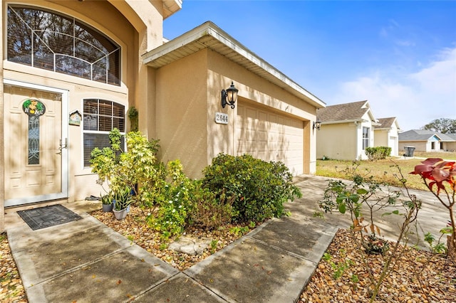 doorway to property featuring a garage, concrete driveway, and stucco siding