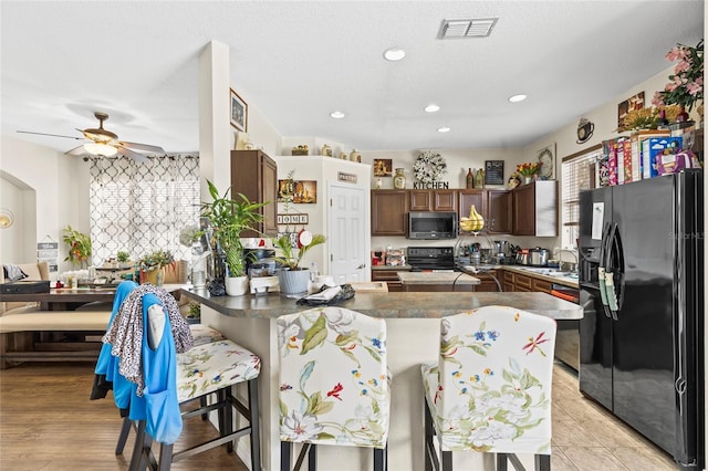 kitchen featuring a breakfast bar area, dark countertops, stainless steel microwave, black refrigerator with ice dispenser, and visible vents