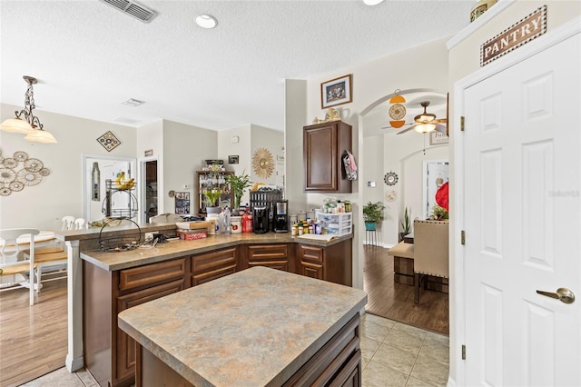 kitchen featuring arched walkways, light tile patterned floors, light countertops, visible vents, and a kitchen island