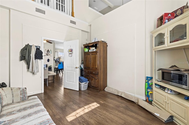 living area with dark wood-type flooring, visible vents, and a towering ceiling