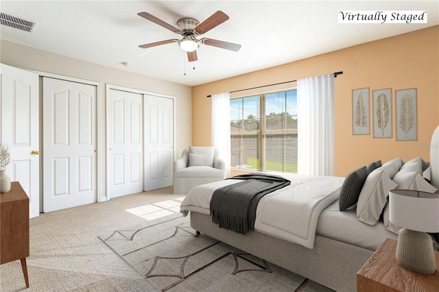 bedroom with ceiling fan, light colored carpet, a textured ceiling, and two closets