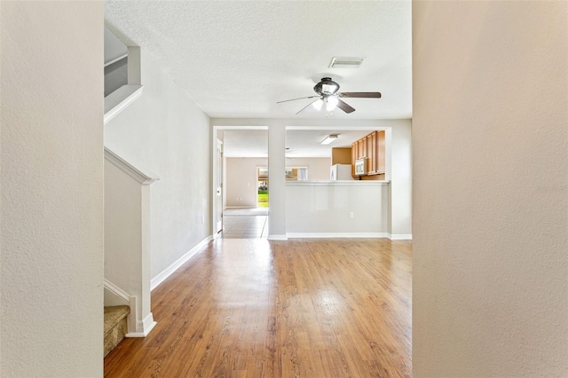 unfurnished living room featuring ceiling fan, light hardwood / wood-style floors, and a textured ceiling