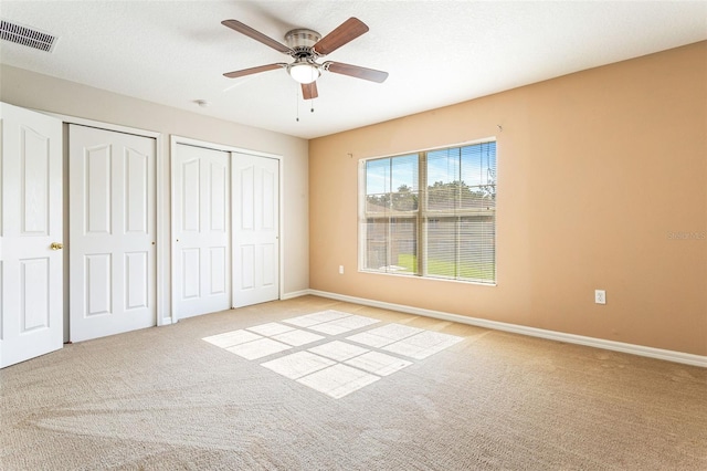 unfurnished bedroom featuring a textured ceiling, ceiling fan, light carpet, and two closets