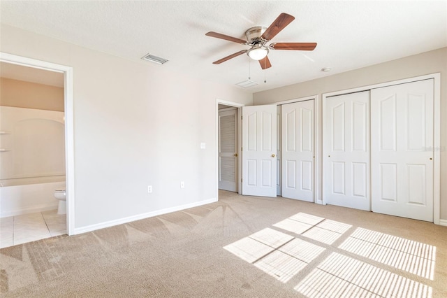 unfurnished bedroom with light carpet, a textured ceiling, two closets, ceiling fan, and connected bathroom