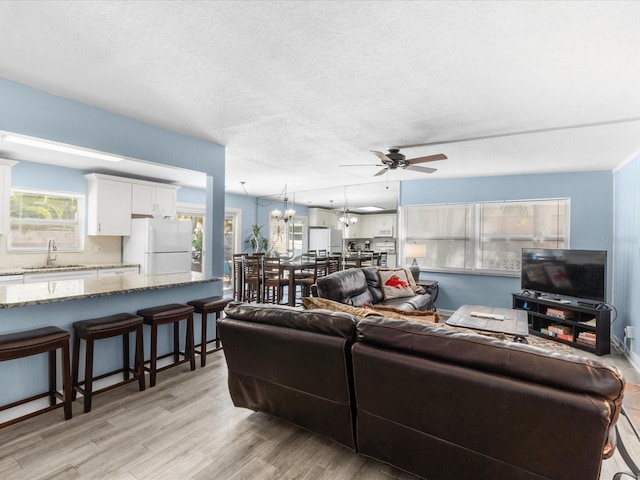 living room featuring a textured ceiling, sink, ceiling fan with notable chandelier, and light wood-type flooring