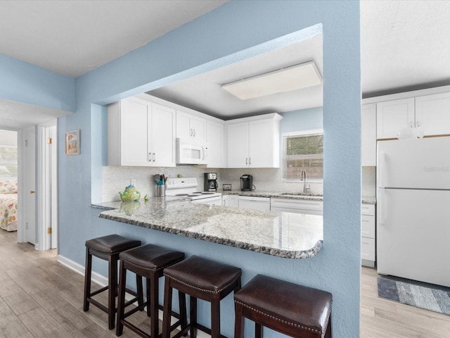 kitchen featuring white appliances, backsplash, sink, light stone counters, and white cabinetry