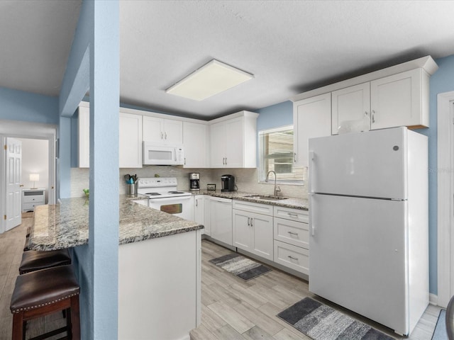 kitchen featuring white cabinets, white appliances, kitchen peninsula, and sink