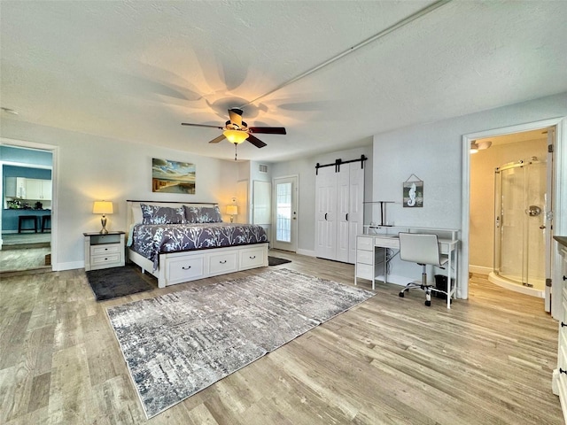 bedroom featuring ceiling fan, a barn door, light hardwood / wood-style floors, and a textured ceiling