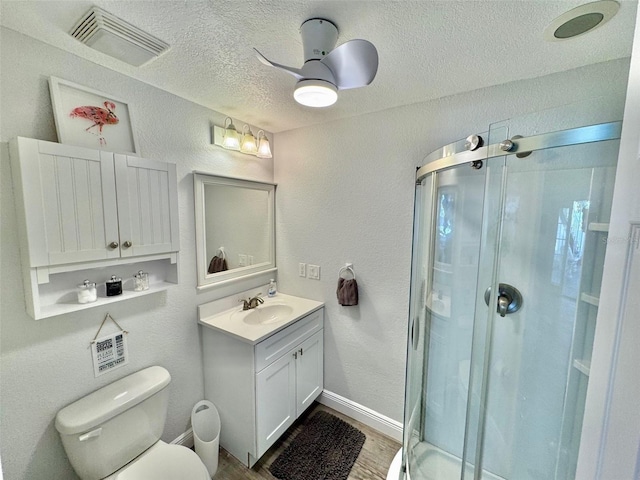 bathroom with ceiling fan, a textured ceiling, toilet, a shower with door, and vanity