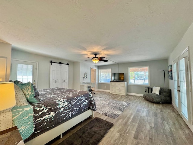 bedroom with a barn door, ceiling fan, light hardwood / wood-style floors, and a textured ceiling