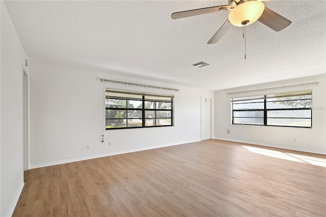 empty room featuring ceiling fan, a healthy amount of sunlight, light wood-type flooring, and a textured ceiling