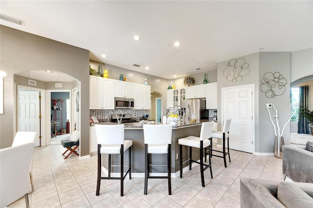 kitchen with white cabinetry, a kitchen breakfast bar, tasteful backsplash, an island with sink, and appliances with stainless steel finishes