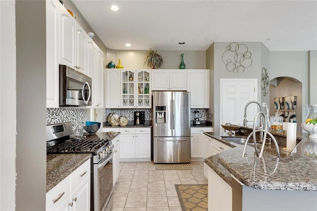 kitchen with appliances with stainless steel finishes, sink, light tile patterned floors, dark stone countertops, and white cabinets