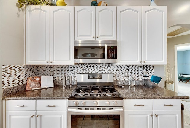 kitchen with white cabinetry, stainless steel appliances, dark stone countertops, decorative backsplash, and light tile patterned floors