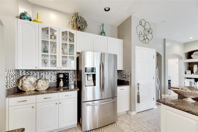 kitchen featuring dark stone countertops, stainless steel fridge, white cabinets, and light tile patterned floors