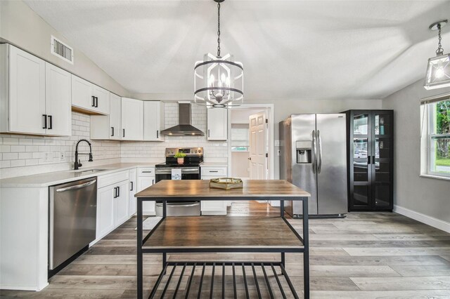 kitchen featuring white cabinets, wall chimney range hood, hanging light fixtures, and appliances with stainless steel finishes