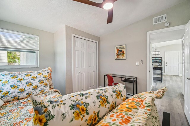 bedroom with a textured ceiling, ceiling fan, wood-type flooring, a closet, and lofted ceiling