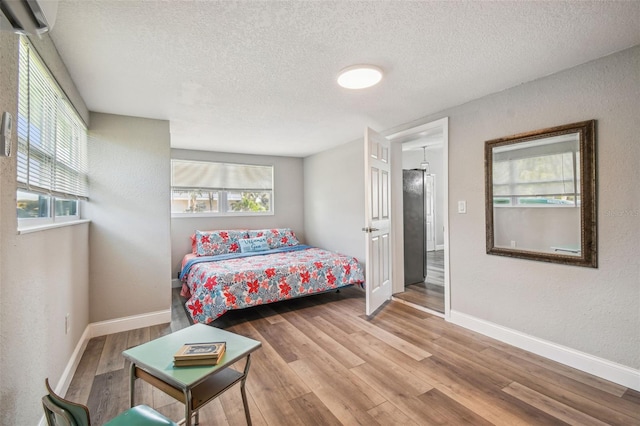 bedroom with a wall mounted air conditioner, a textured ceiling, and light wood-type flooring