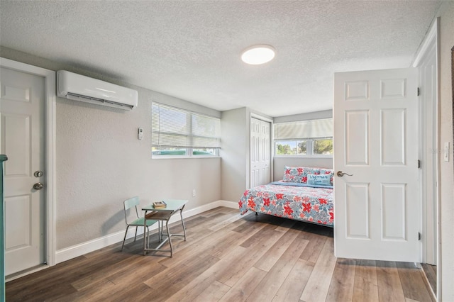 bedroom featuring a wall mounted air conditioner, wood-type flooring, a textured ceiling, and a closet