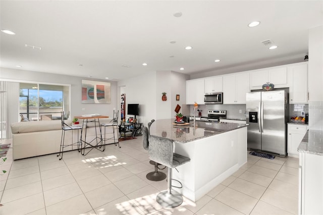 kitchen with light tile patterned floors, appliances with stainless steel finishes, stone countertops, a kitchen bar, and white cabinetry