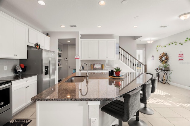 kitchen featuring a center island with sink, tasteful backsplash, dark stone counters, and sink