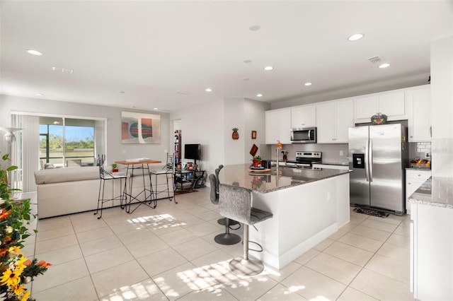 kitchen featuring stainless steel appliances, dark stone counters, a breakfast bar, white cabinets, and a center island with sink