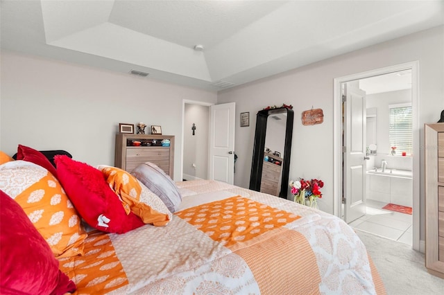 bedroom featuring a tray ceiling, connected bathroom, and light carpet