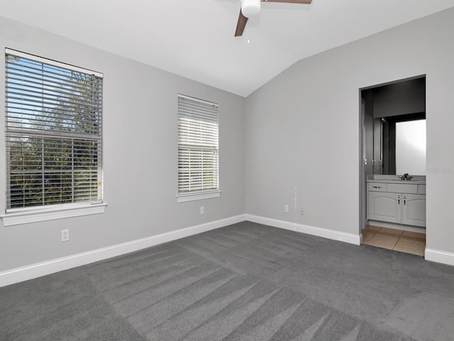 unfurnished bedroom with multiple windows, ceiling fan, vaulted ceiling, and dark colored carpet