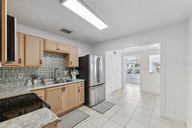 kitchen featuring a sink, visible vents, freestanding refrigerator, backsplash, and light brown cabinets