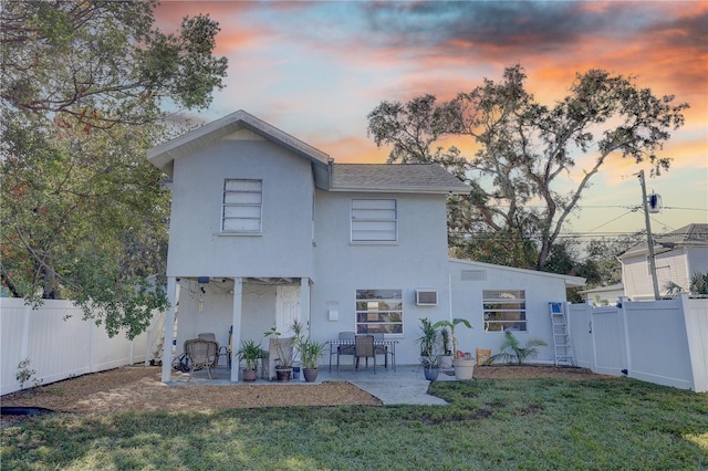 back house at dusk featuring a patio and a lawn