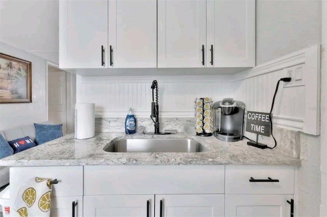 interior details with white cabinets, light stone countertops, and sink