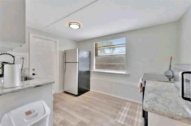 kitchen with light stone countertops, stainless steel fridge, light wood-type flooring, white cabinets, and range