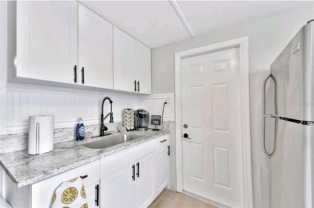 kitchen featuring white cabinets, light stone countertops, sink, and stainless steel refrigerator