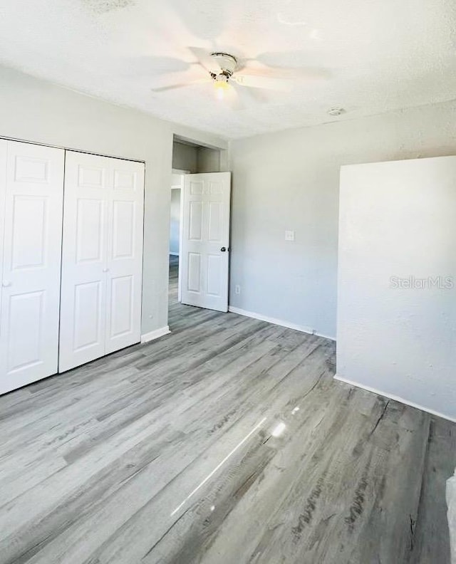 unfurnished bedroom featuring ceiling fan, a closet, a textured ceiling, and light wood-type flooring