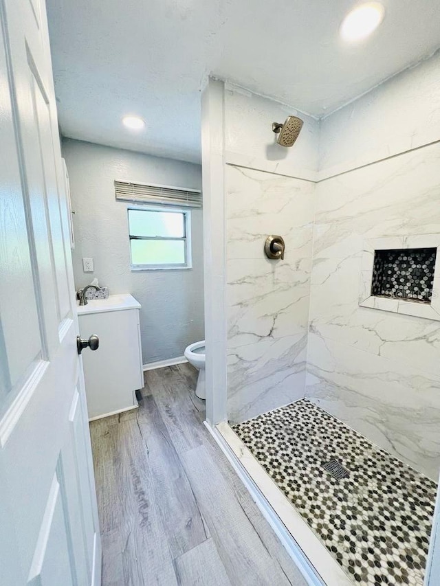 bathroom with a tile shower, toilet, and hardwood / wood-style flooring