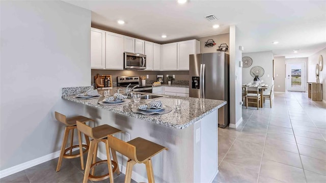 kitchen featuring a kitchen breakfast bar, kitchen peninsula, light tile patterned floors, white cabinetry, and stainless steel appliances