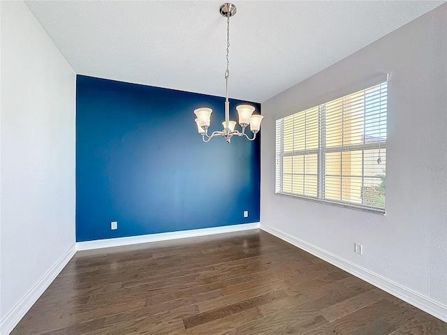 spare room with dark wood-type flooring and a chandelier