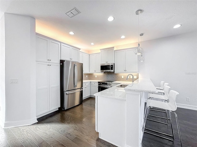 kitchen with white cabinetry, sink, hanging light fixtures, kitchen peninsula, and appliances with stainless steel finishes