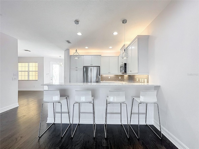 kitchen featuring dark wood-type flooring, stainless steel appliances, kitchen peninsula, decorative light fixtures, and white cabinets