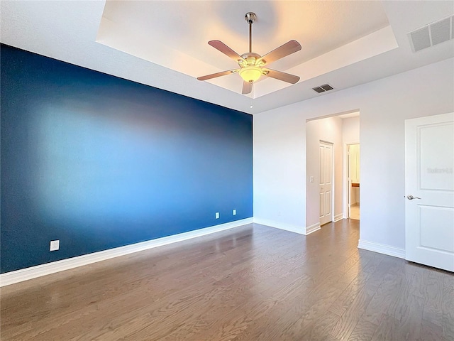 spare room with ceiling fan, a raised ceiling, and wood-type flooring