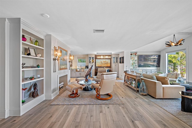 living room featuring a chandelier, a textured ceiling, light hardwood / wood-style floors, and built in features