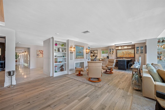 living room with built in features, a textured ceiling, bar, and light hardwood / wood-style flooring