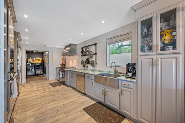 kitchen featuring gray cabinetry, wall chimney range hood, sink, light wood-type flooring, and appliances with stainless steel finishes