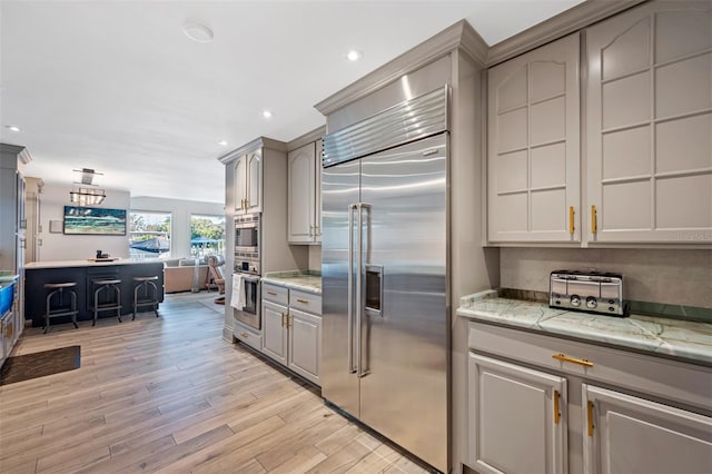 kitchen featuring gray cabinetry, light stone countertops, appliances with stainless steel finishes, and light hardwood / wood-style flooring