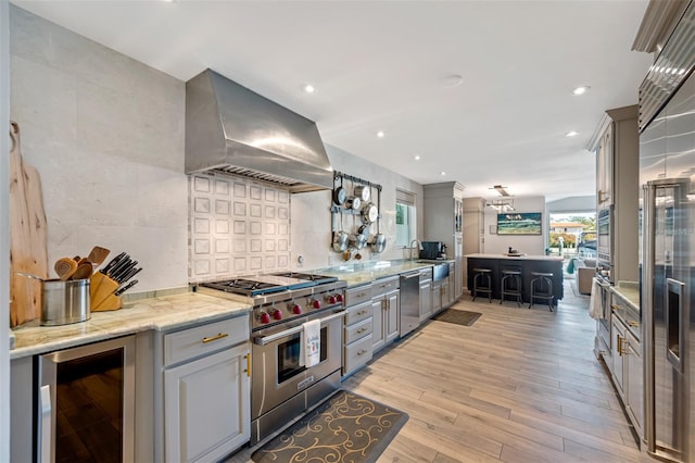 kitchen with wall chimney exhaust hood, wine cooler, stainless steel appliances, and a wealth of natural light