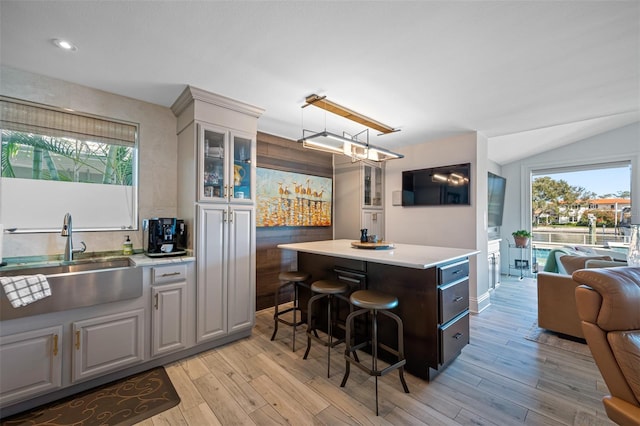 kitchen with a center island, sink, light wood-type flooring, a healthy amount of sunlight, and a breakfast bar area