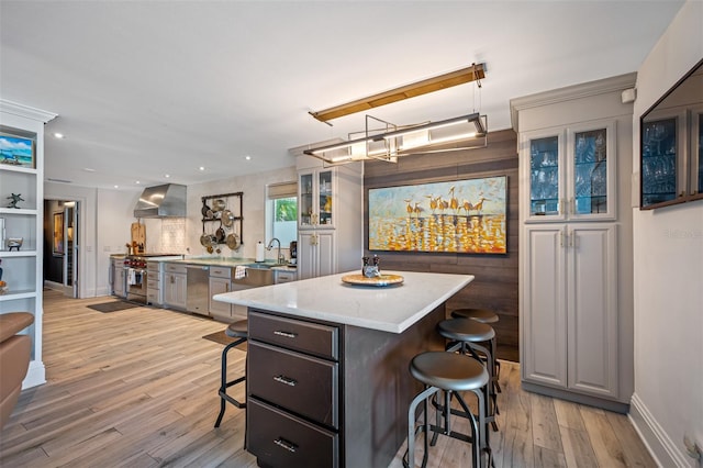 kitchen with a breakfast bar, light wood-type flooring, a center island, and wall chimney range hood