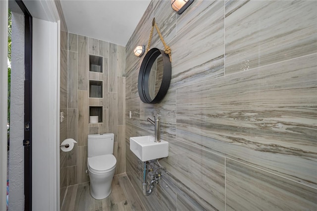 bathroom featuring sink, toilet, wood-type flooring, and tile walls