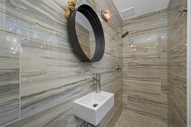 bathroom featuring a tile shower, sink, and tile walls