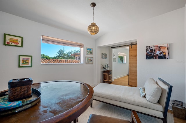 sitting room with wood-type flooring, a barn door, and lofted ceiling